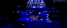 a woman with pink hair is standing on a stage in front of a blue light .