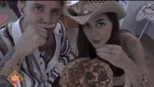 a man in a cowboy hat and a woman in a striped shirt eating a pizza