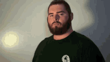 a man with a beard is wearing a black t-shirt and looking at the camera .