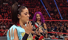 a female wrestler with purple hair is holding a microphone in front of a crowd .