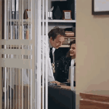 a man in a lab coat is talking to a woman behind a glass door