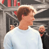a man wearing a light blue nike sweatshirt is smiling in front of a sign that says # ibi25
