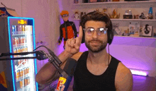 a man wearing headphones and glasses is giving a peace sign in front of a microphone in a room .