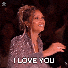 a woman in a silver dress is saying i love you in front of a crowd .