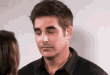 a man in a black shirt is standing next to a woman and looking down .