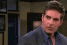 a man in a suit and blue shirt is standing in a room and making a funny face .