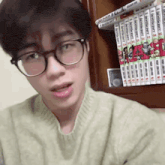 a young man wearing glasses is standing in front of a bookshelf .