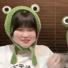 a girl wearing a green frog hat is sitting in front of a window .