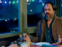 a man with a beard sitting at a table with a plate of food