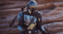 a man in armor is standing in front of a rock wall holding a gun