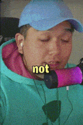 a man wearing a blue hat and a green hoodie is singing into a pink and purple microphone with the word not on his face