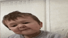 a young boy is making a funny face while sitting in front of a window .