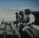 three men sit at a wooden picnic table with plates of food on it