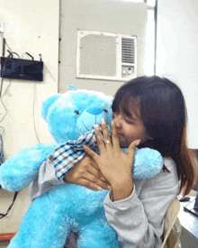 a woman is holding a blue teddy bear with a plaid shirt on