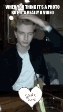 a man is sitting at a table with a drink and a heart that says " you 're dumb "