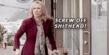 a woman is standing in front of a door with the words `` screw off shithead '' on it .
