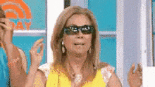a woman wearing sunglasses and a yellow shirt is clapping her hands