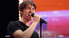 a young man singing into a microphone with a nbc logo in the background