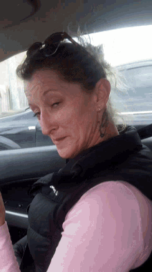 a woman with a tattoo on her face is wearing a pink shirt and black vest