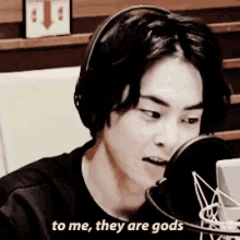 a man wearing headphones is talking into a microphone with the words to me they are gods written below him