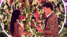 a man and a woman are standing next to each other in front of a flower wall .