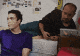 a man in a purple shirt sits next to a man in a black shirt