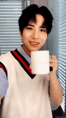 a young man in a vest is holding a cup of coffee and smiling