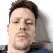 a man with a beard is sitting on a couch with his hand on his chin .