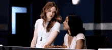 two women are sitting at a desk talking to each other in a dark room .
