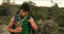 a man wearing a green and black striped shirt and a backpack is holding a snake