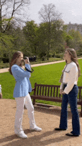 a woman taking a picture of another woman in a park with a camera