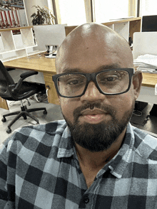 a man wearing glasses and a plaid shirt is sitting in front of a desk