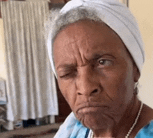 an older woman wearing a white turban and a blue shirt is making a funny face .