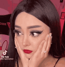 a woman wearing a wig and a ring is holding her face with her hands .