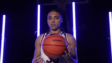 a woman in a uconn jersey is holding a basketball in her hands .