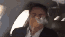 a man in a suit is smoking a cigarette in the back seat of a car .