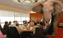 a group of people are sitting around a table with an elephant in the middle