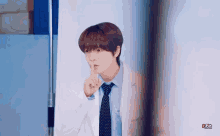 a young man in a white coat and tie is holding his finger to his mouth .