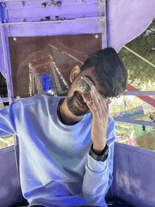 a man wearing glasses and a blue shirt is covering his eyes with his hand