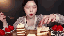 a woman is eating a slice of cake with strawberries on the side