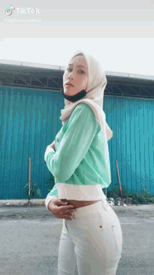 a woman wearing a hijab is standing in front of a blue building .