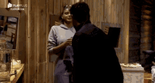 a man and a woman are kissing in front of a wooden wall with playplus written on it .