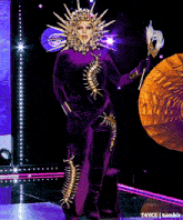 a woman in a purple and gold costume is holding a feather mask