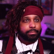 a man with a beard and dreadlocks is wearing a red headband and a suit .