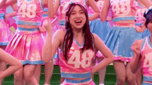a group of cheerleaders wearing pink and blue uniforms with the number 48 on them are dancing on a field .