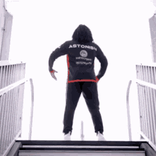 a person wearing a black and red astonish jacket stands on a set of stairs