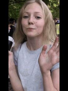 a girl with blonde hair and blue eyes is waving her hands