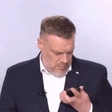 a man in a suit and white shirt is looking at his cell phone .