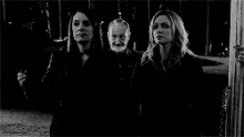 a black and white photo of a man and two women standing next to each other in a dark room .