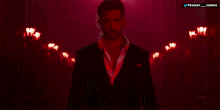 a man in a suit and white shirt is standing in a dark room with red lights behind him and the words pranay varma above him